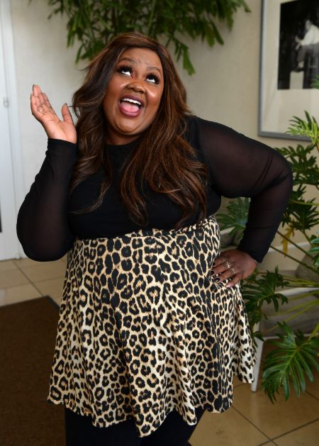 Nicole Byer in a black dress poses for a picture.